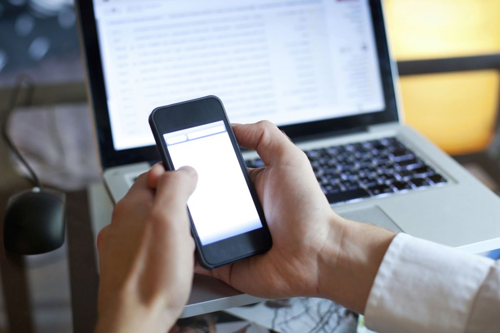 hombre-manejando-su-smartphone-frente-a-su-ordenador